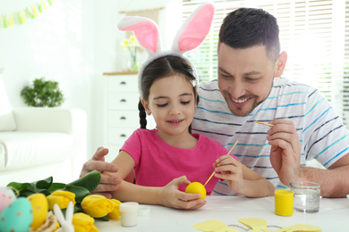 Happy daughter with bunny ears headband and her father painting Easter egg at home