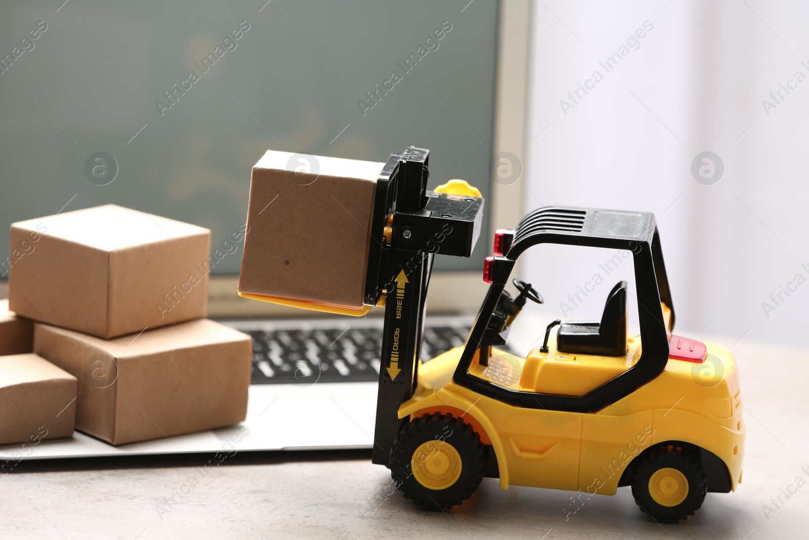 Photo of Toy forklift with box near laptop on table. Logistics and wholesale concept