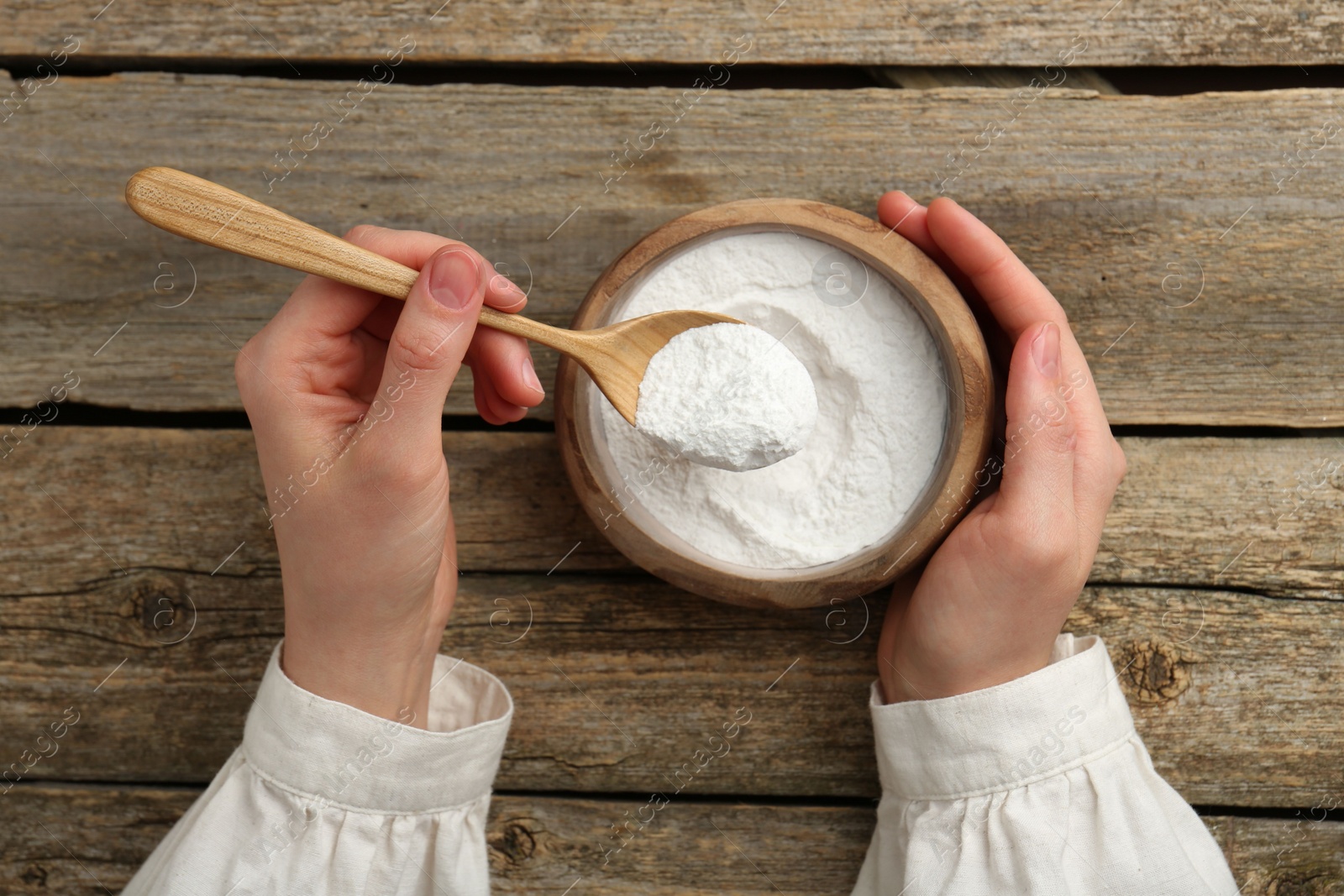 Photo of Woman taking baking powder with spoon from bowl at wooden table, top view