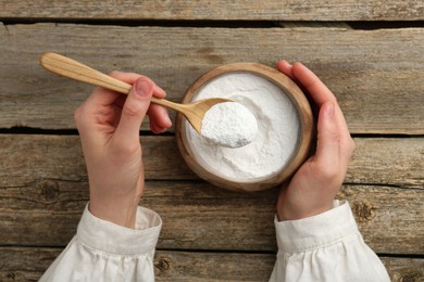 Photo of Woman taking baking powder with spoon from bowl at wooden table, top view