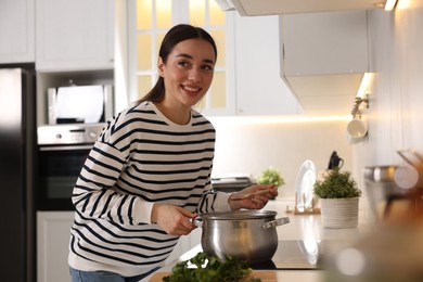 Photo of Smiling woman with wooden spoon cooking soup in kitchen