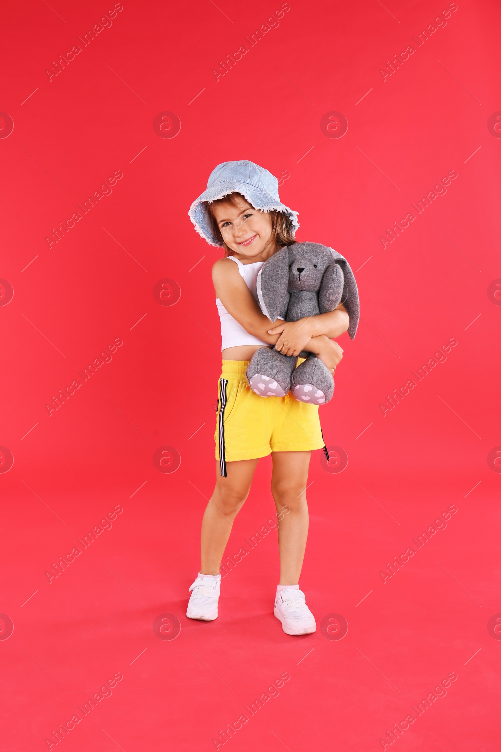 Photo of Cute little girl with toy rabbit on red background