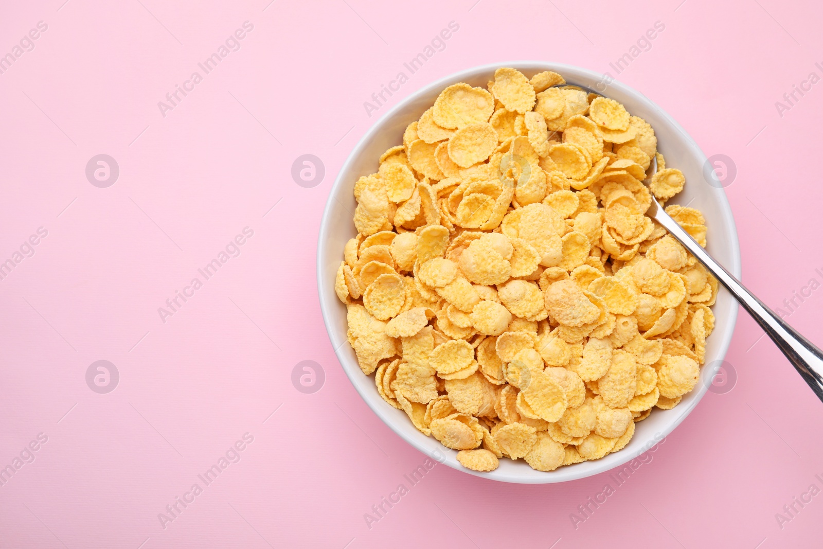 Photo of Breakfast cereal. Tasty corn flakes in bowl and spoon on pink table, top view. Space for text