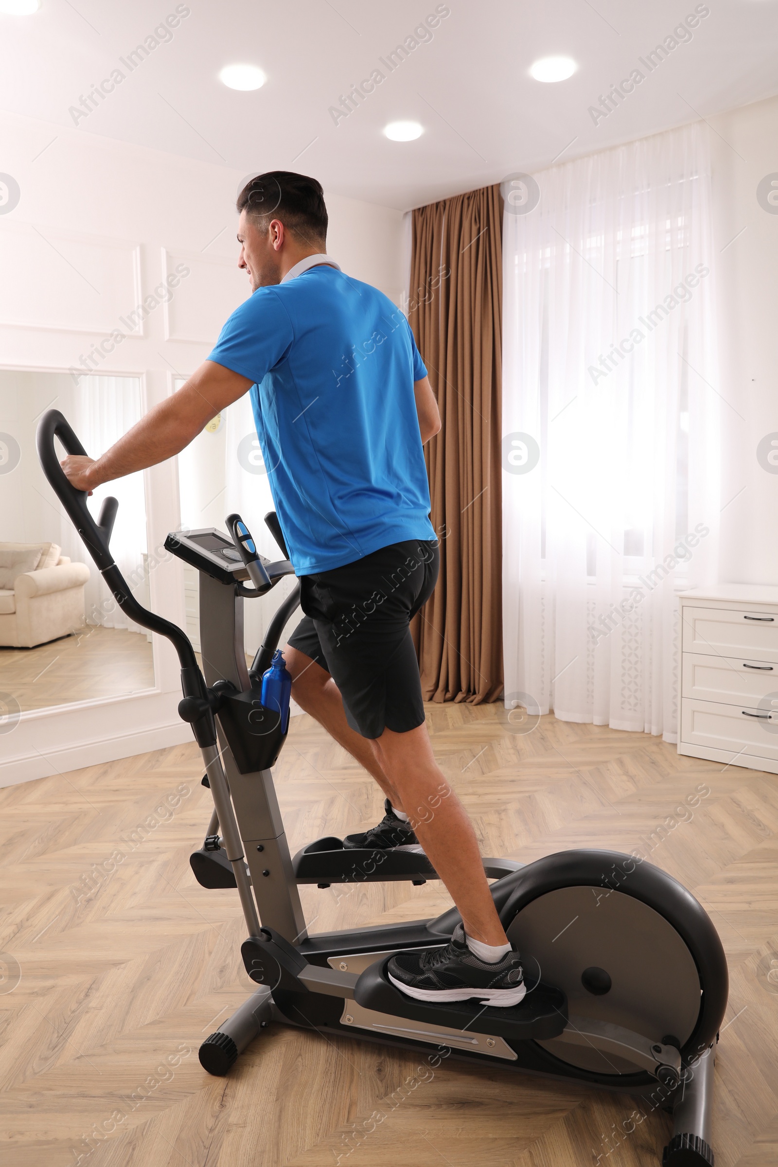 Photo of Man with headphones using modern elliptical machine at home