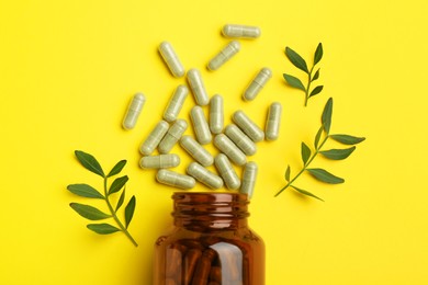 Photo of Vitamin pills, branches and bottle on yellow background, flat lay