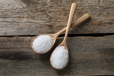 Organic salt in spoons on wooden table, flat lay