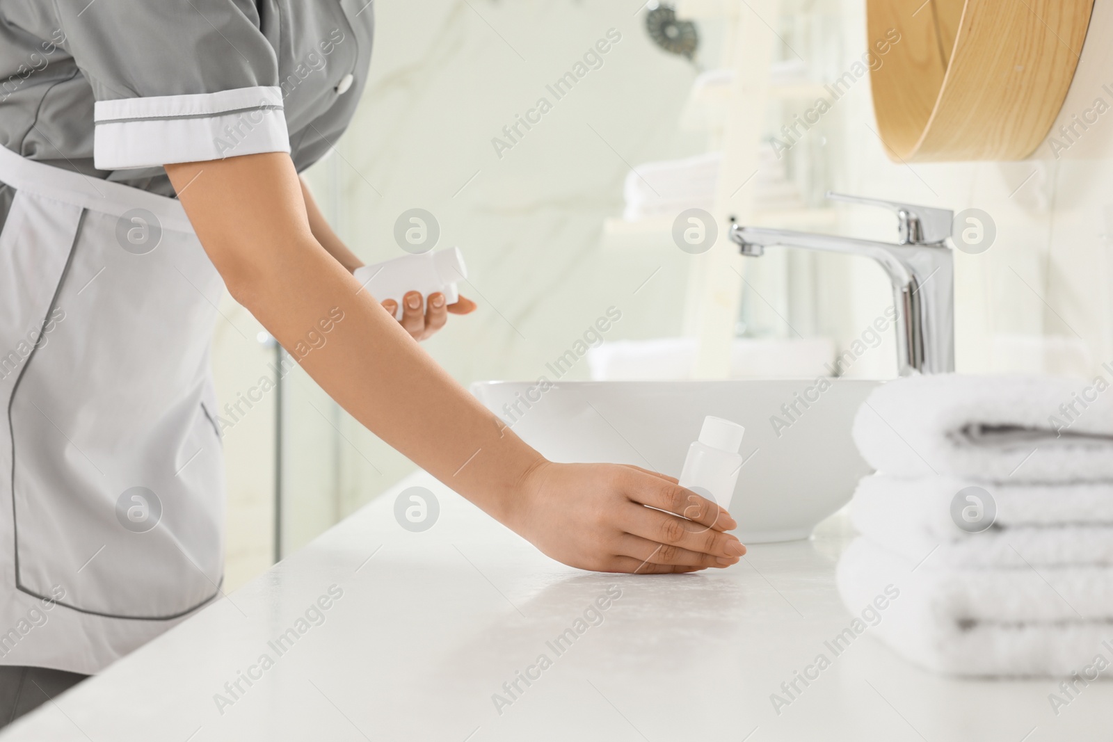 Photo of Chambermaid putting bottle of shampoo on bathroom counter in hotel, closeup
