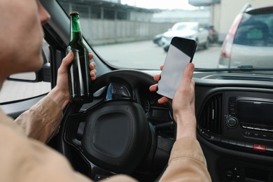 Photo of Man with bottle of beer and smartphone in car, closeup. Don't drink and drive concept