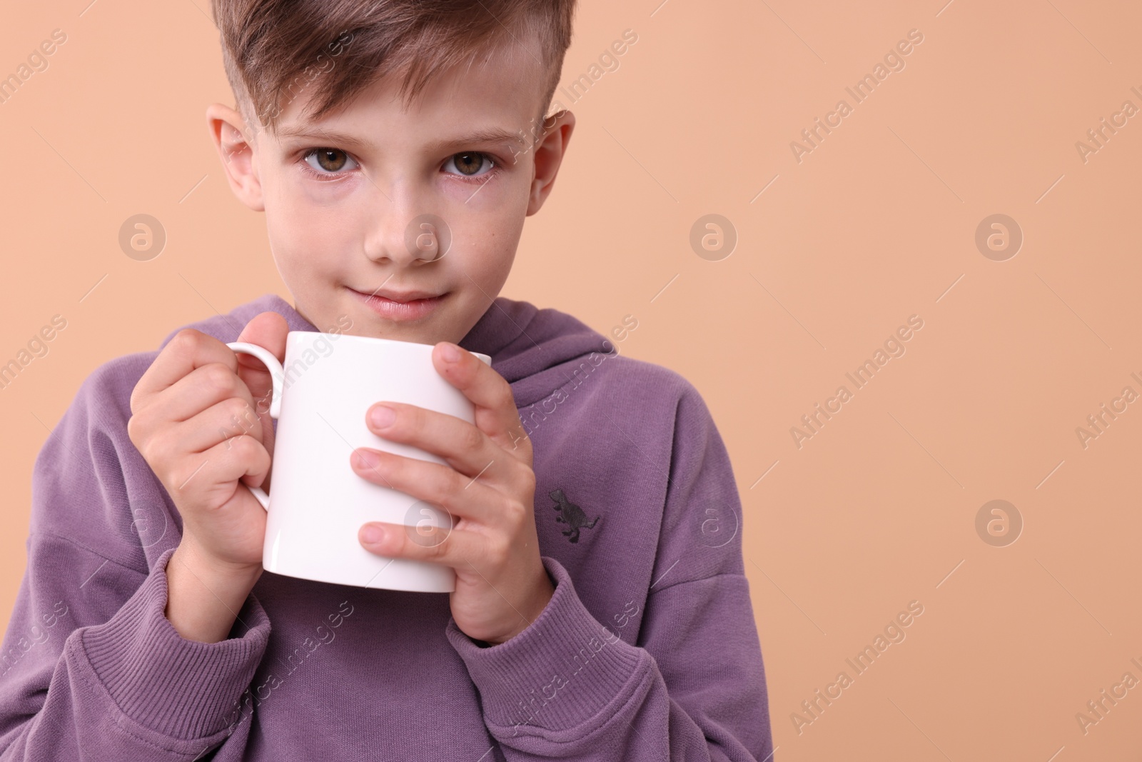 Photo of Cute boy with white ceramic mug on beige background, space for text