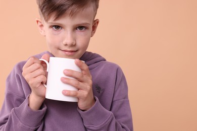 Cute boy with white ceramic mug on beige background, space for text