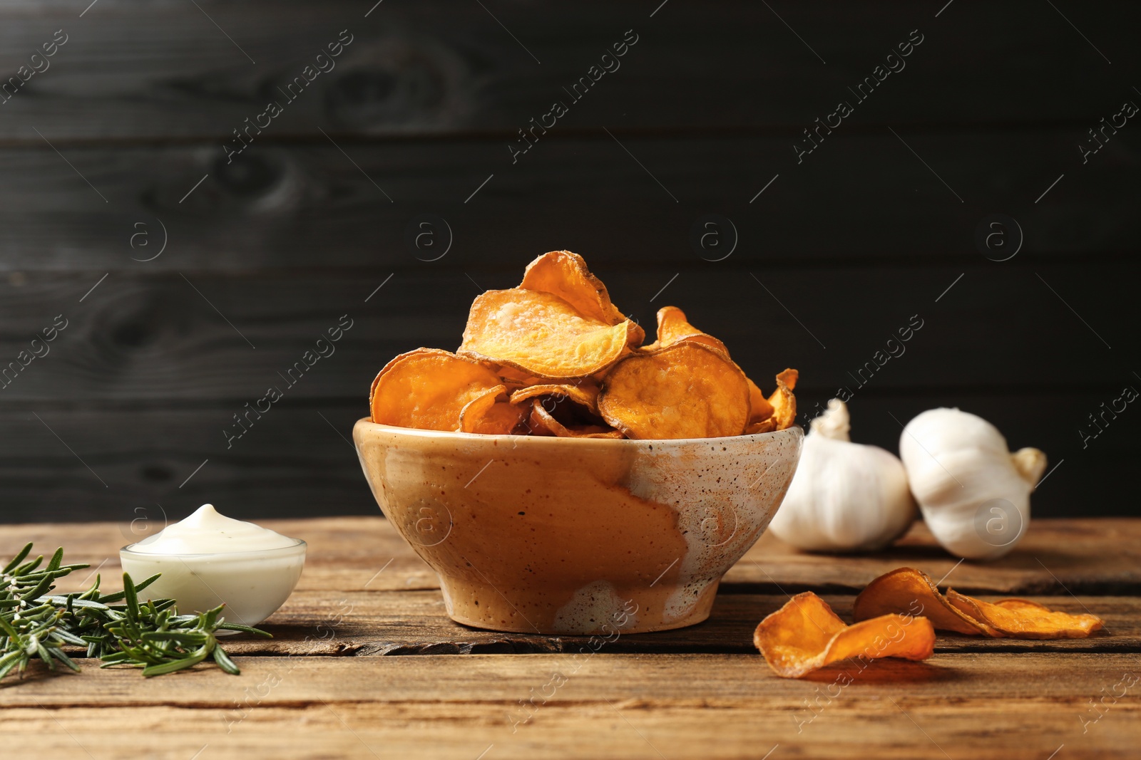 Photo of Delicious sweet potato chips in bowl, rosemary and sauce on table