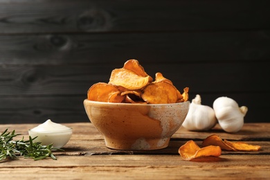 Delicious sweet potato chips in bowl, rosemary and sauce on table