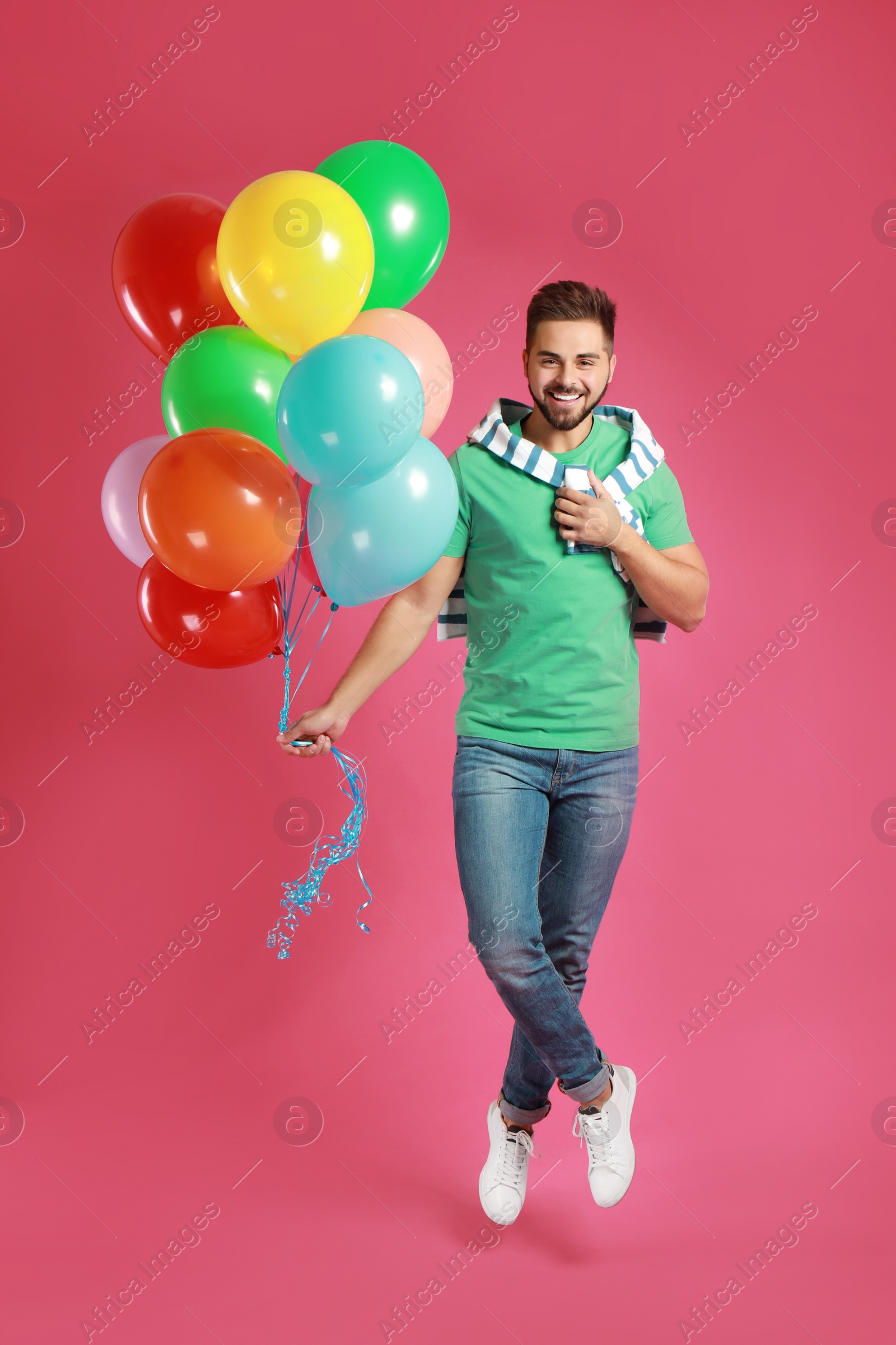 Photo of Young man jumping with bunch of colorful balloons on pink background