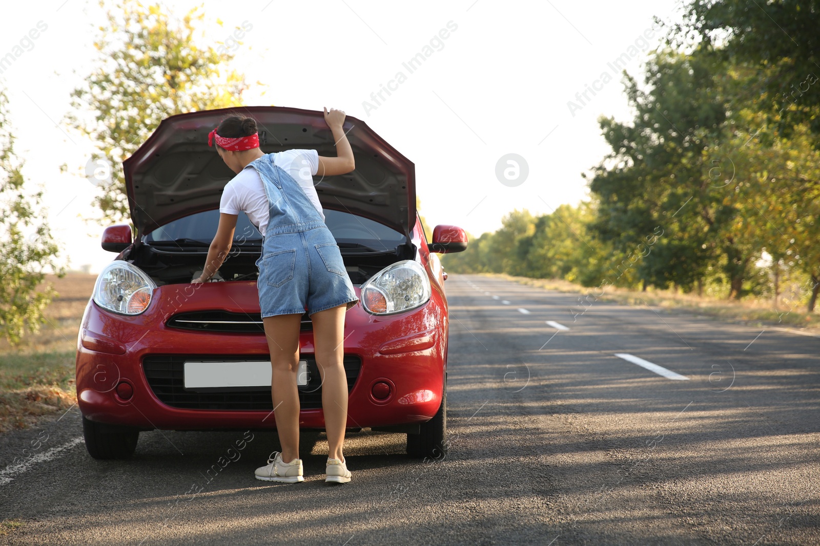 Photo of Young woman fixing broken car outdoors, back view