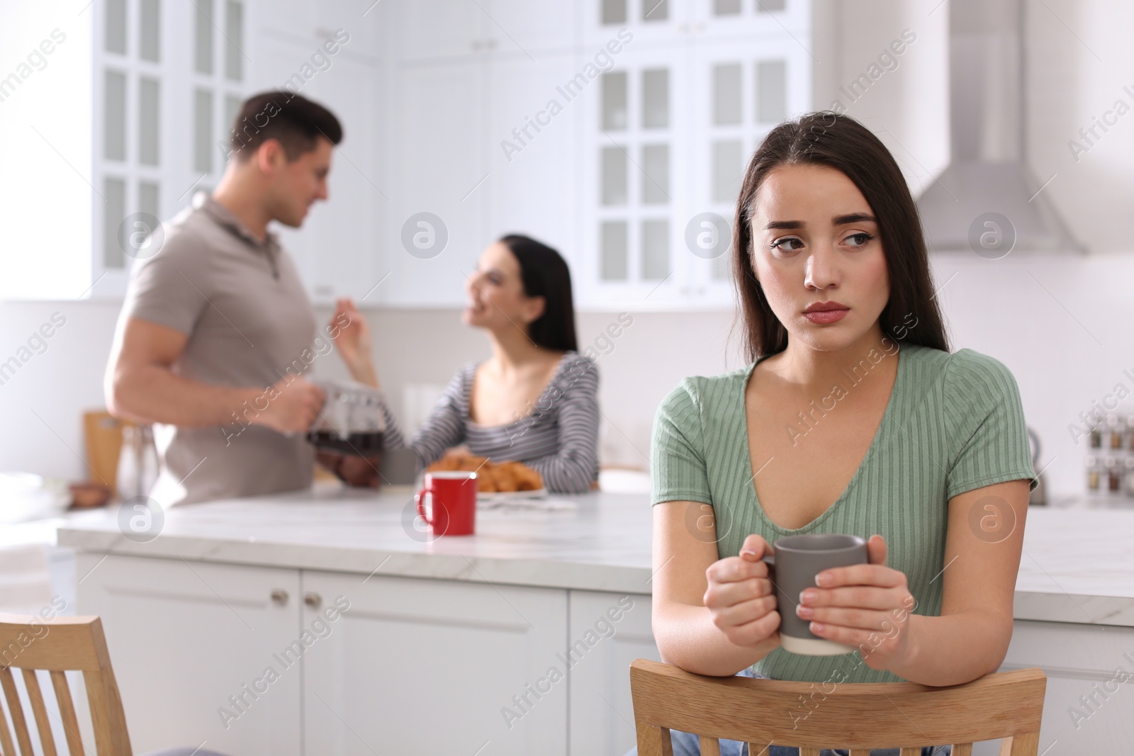 Photo of Unhappy woman feeling jealous while couple spending time together in kitchen