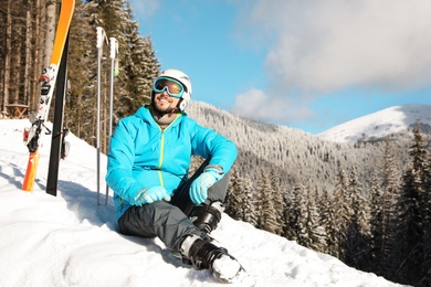Photo of Man with ski equipment sitting on snow in mountains. Winter vacation