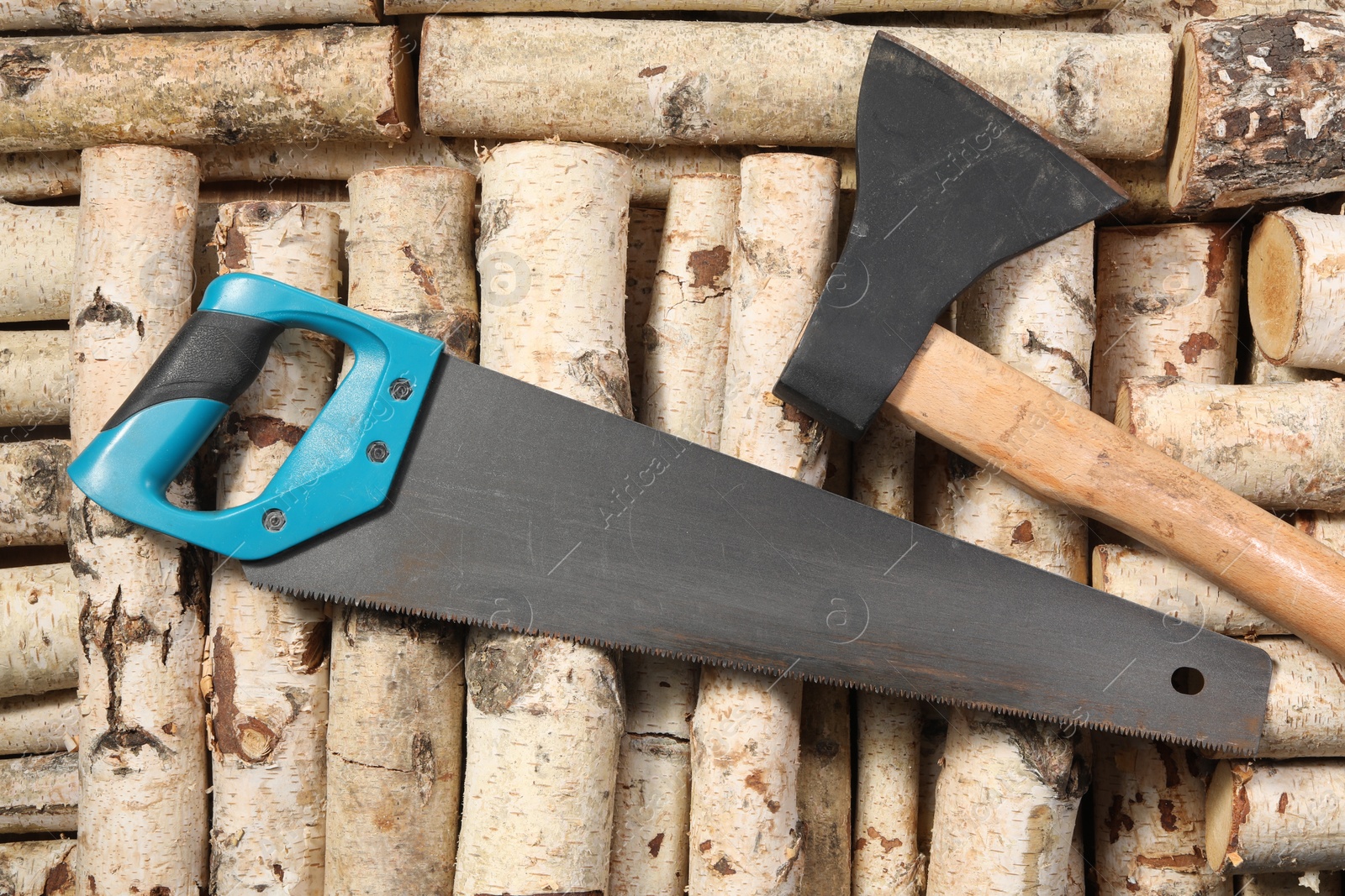 Photo of Saw with light blue handle and axe on firewood, flat lay