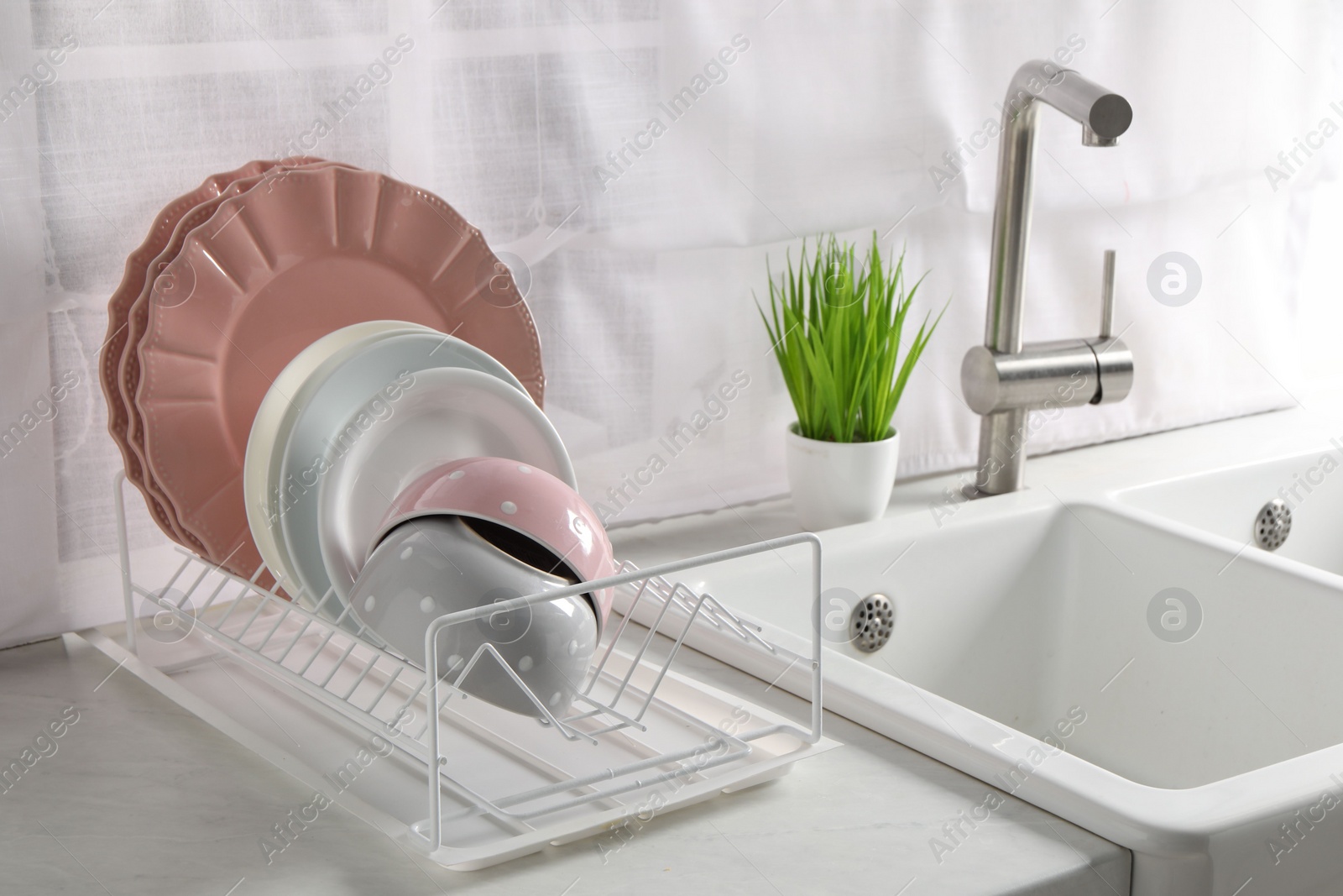 Photo of Drainer with different clean dishware on white table in kitchen