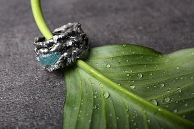 Photo of Beautiful silver ring with apatite gemstone and green leaf on grey background
