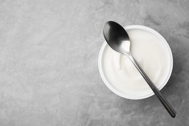 Photo of Delicious natural yogurt in plastic cup and spoon on grey table, top view. Space for text