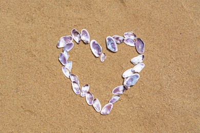 Photo of Heart made with beautiful sea shells on wet sand, flat lay