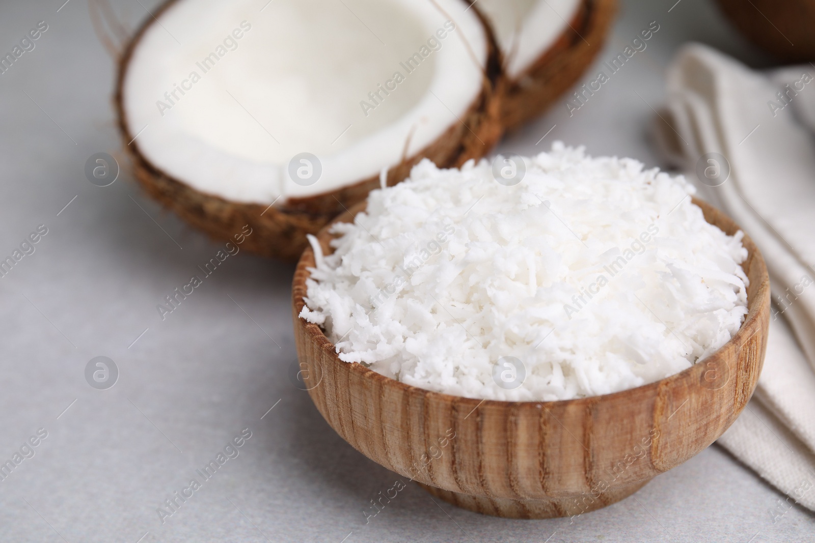 Photo of Coconut flakes in bowl and nut on light grey table, closeup