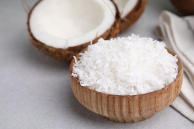 Photo of Coconut flakes in bowl and nut on light grey table, closeup