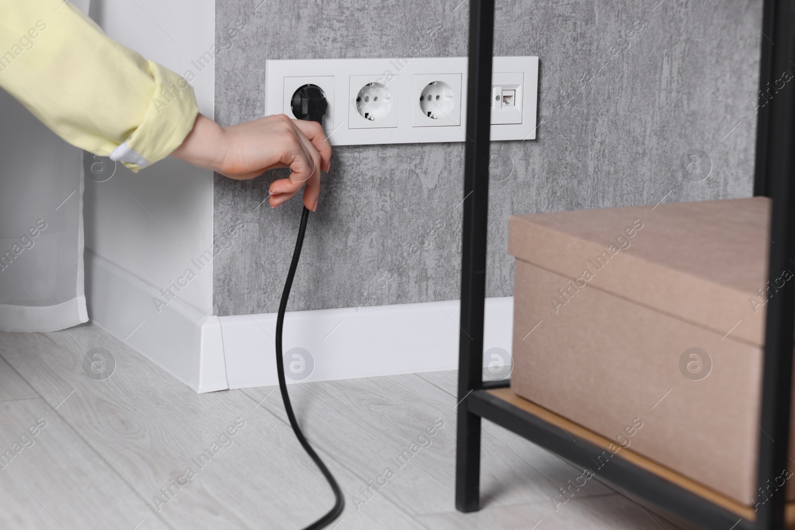 Photo of Woman inserting electric plug into power socket on grey wall indoors, closeup