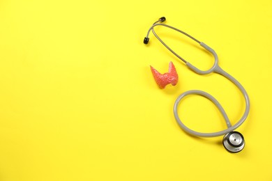 Photo of Endocrinology. Stethoscope and model of thyroid gland on yellow background, top view. Space for text