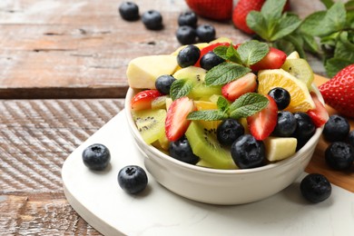 Photo of Tasty fruit salad in bowl and ingredients on wooden table, closeup. Space for text