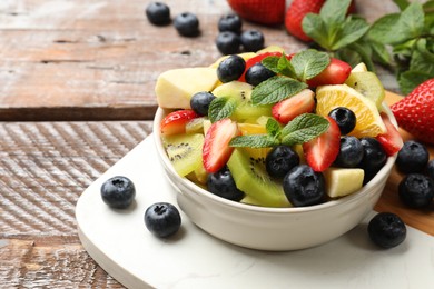 Tasty fruit salad in bowl and ingredients on wooden table, closeup. Space for text