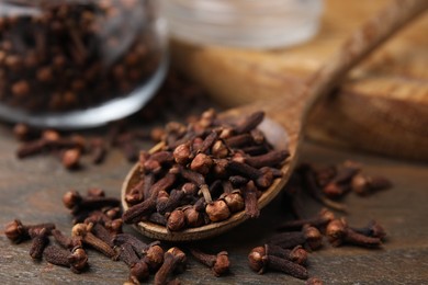 Spoon with aromatic cloves on wooden table, closeup