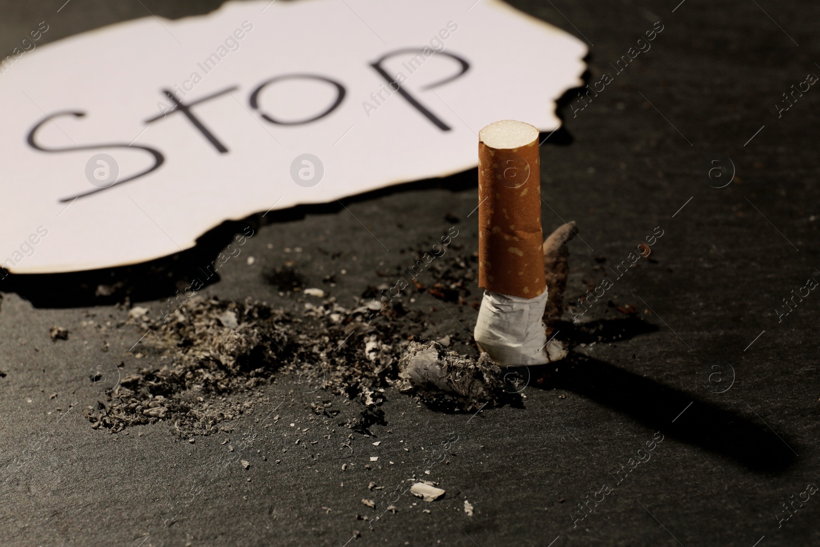 Photo of Burnt cigarette and word Stop written on paper on black table, closeup. No smoking concept