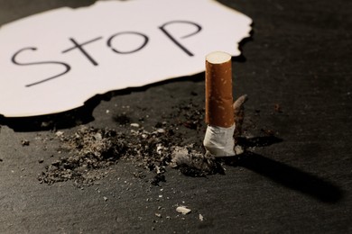 Burnt cigarette and word Stop written on paper on black table, closeup. No smoking concept