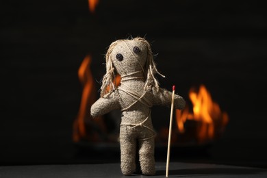 Photo of Voodoo doll with match on black table against blurred flame. Curse ceremony