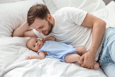 Photo of Father with his cute baby on bed indoors