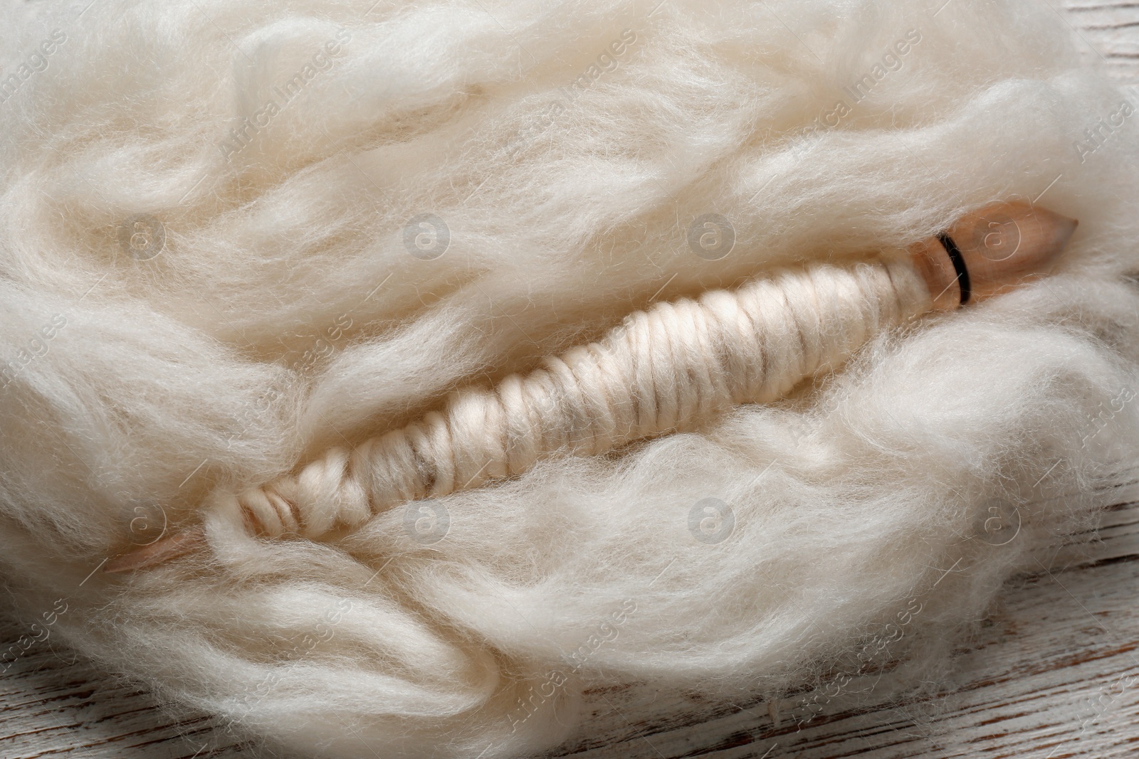 Photo of Soft white wool and spindle on wooden table, closeup