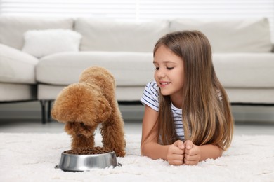 Photo of Little child feeding cute puppy on carpet at home. Lovely pet