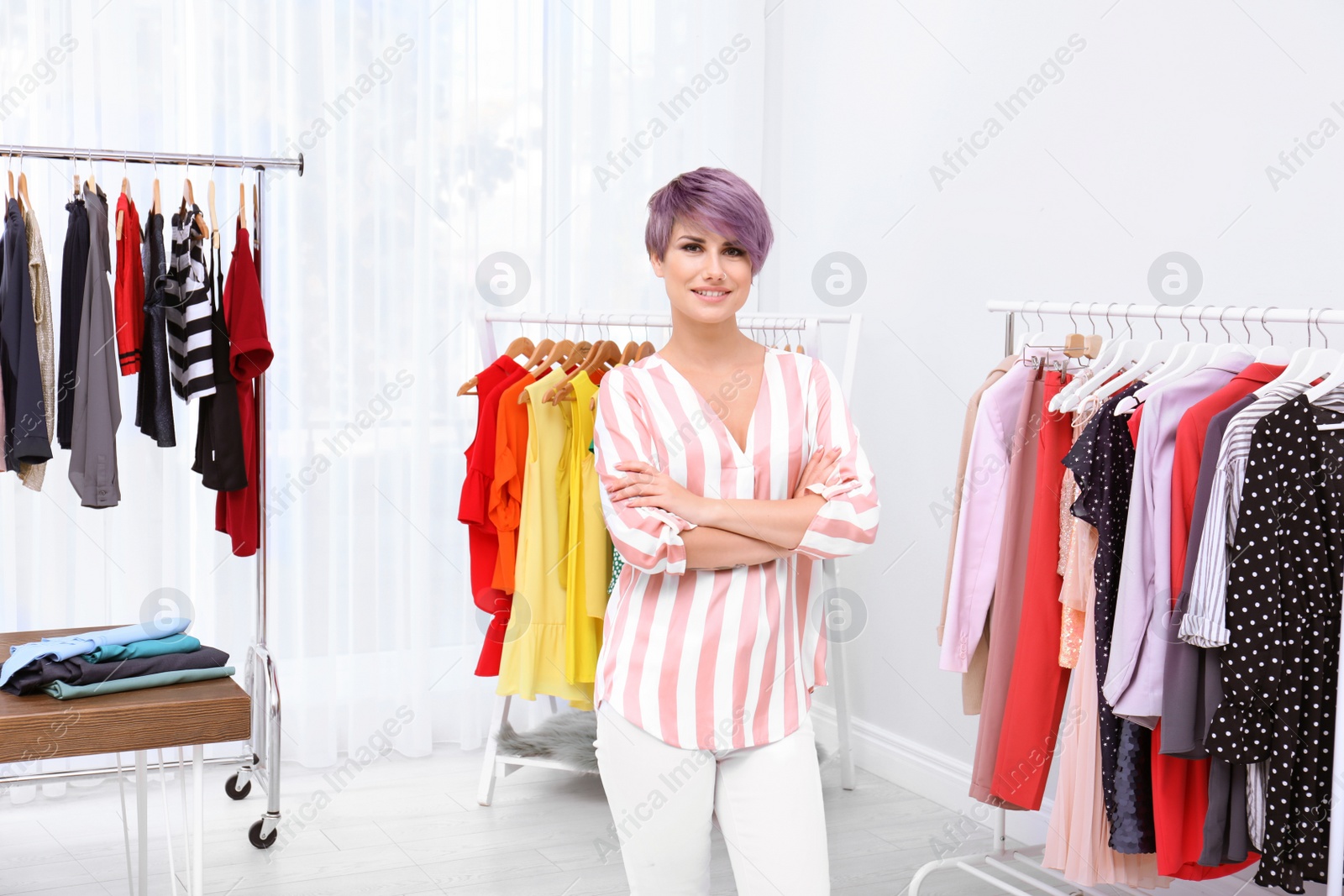 Photo of Beautiful young stylist at workplace near rack with clothes