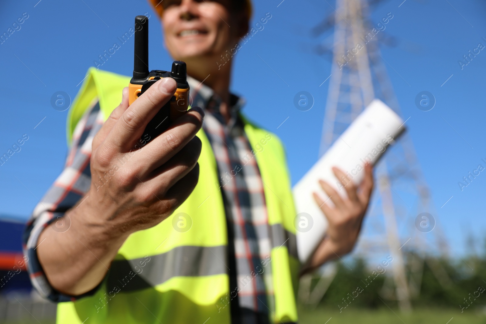 Photo of Professional electrician with portable radio station near high voltage tower, closeup