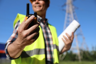 Professional electrician with portable radio station near high voltage tower, closeup