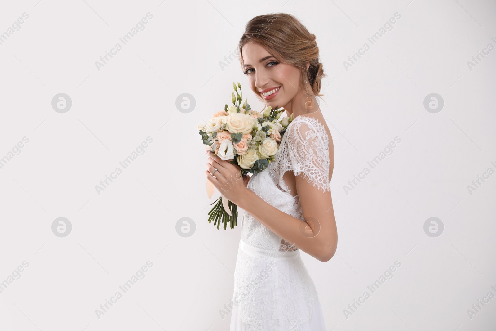 Photo of Young bride with elegant hairstyle holding wedding bouquet on white background