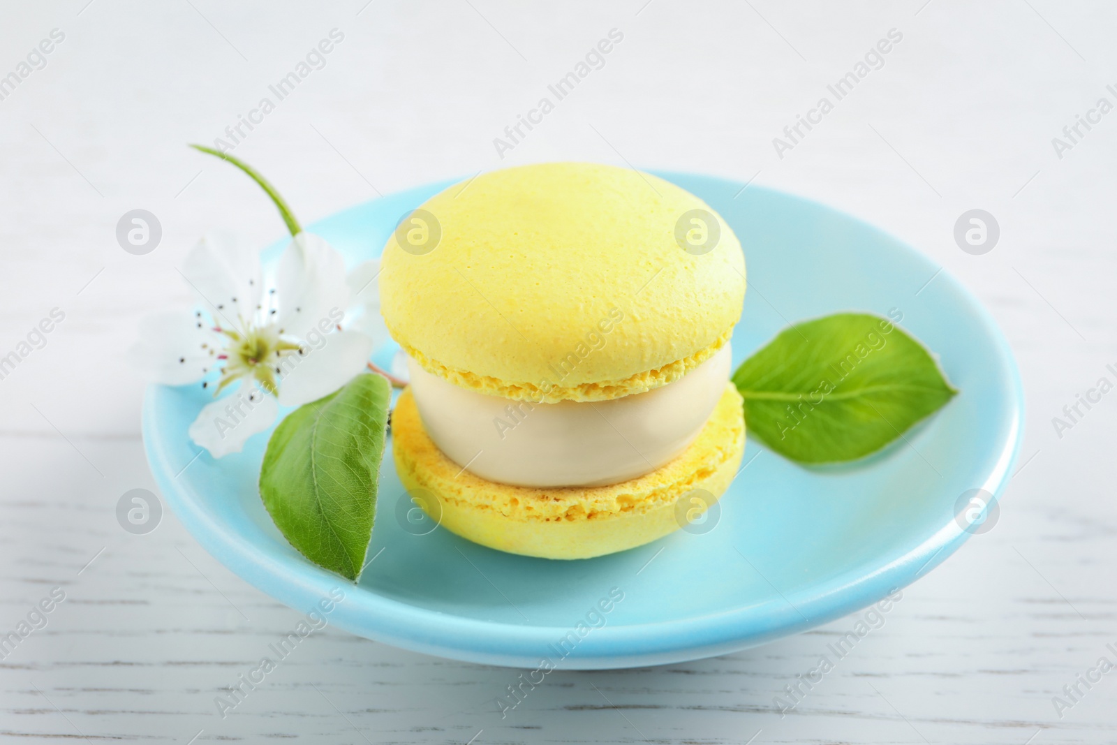 Photo of Delicious yellow macaron and flower on white wooden table, closeup