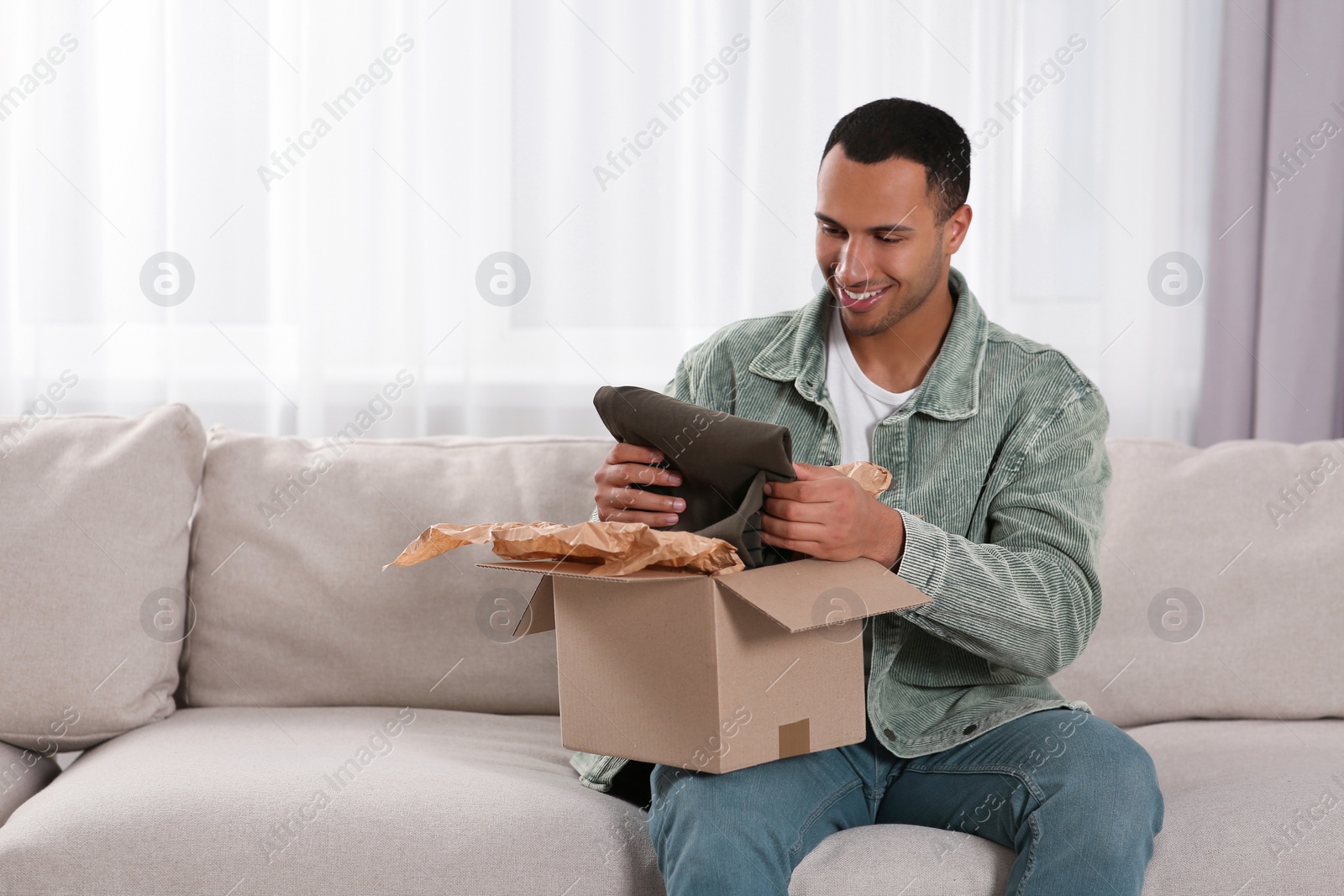 Photo of Happy young man opening parcel at home. Internet shopping