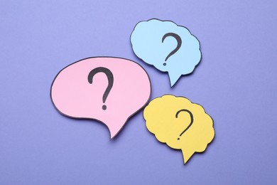 Photo of Different paper speech bubbles with question marks on violet background, flat lay
