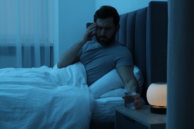 Photo of Man with glass of water suffering from headache in bed at night