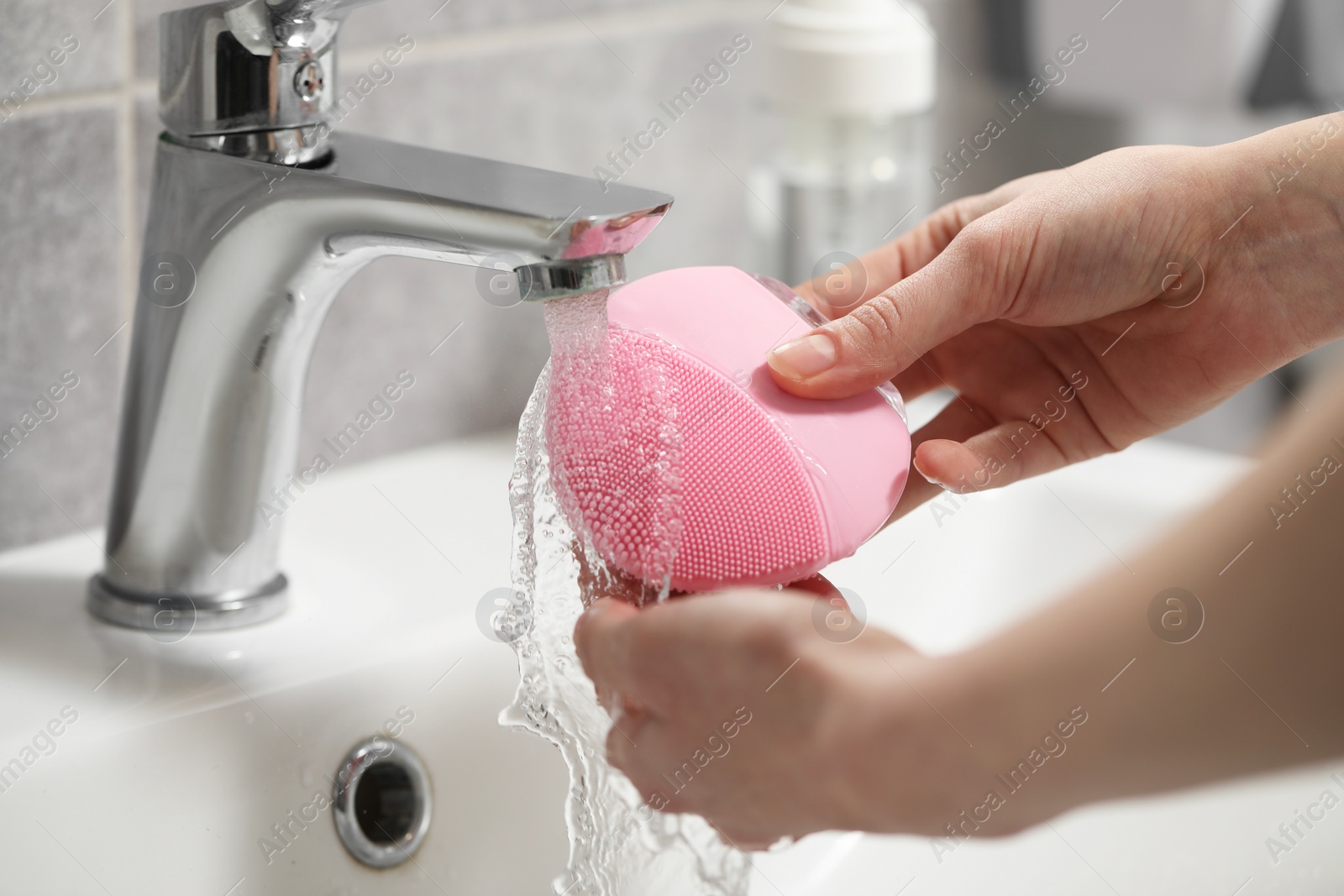 Photo of Young woman washing facial brush in bathroom, closeup