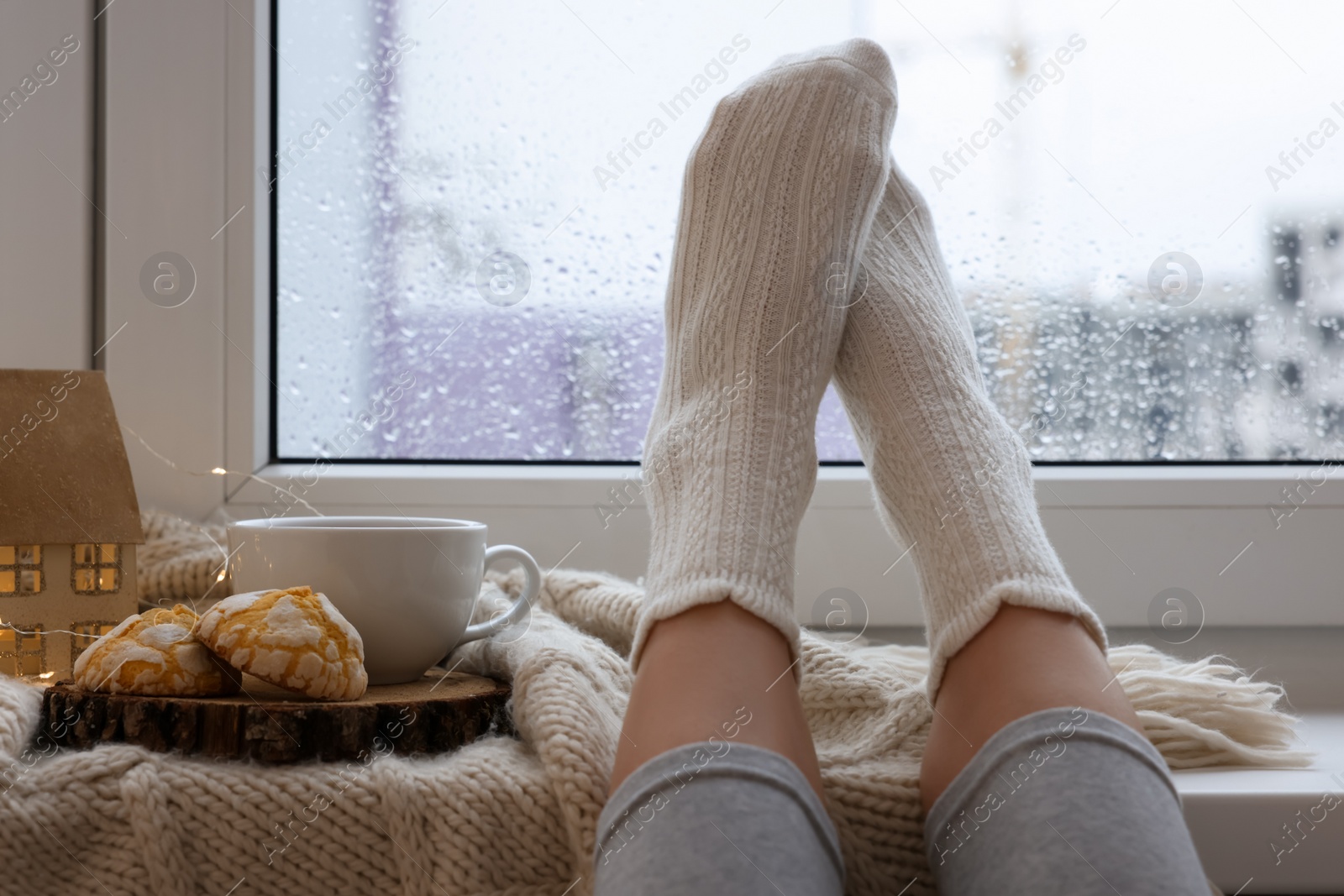 Photo of Woman in knitted socks relaxing near window at home, closeup. Space for text