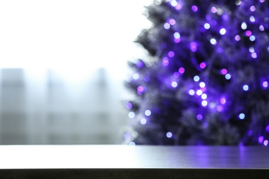 Photo of Blurred view of beautiful Christmas tree with purple lights near window indoors, focus on table. Space for text