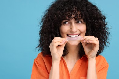 Young woman applying whitening strip on her teeth against light blue background, space for text